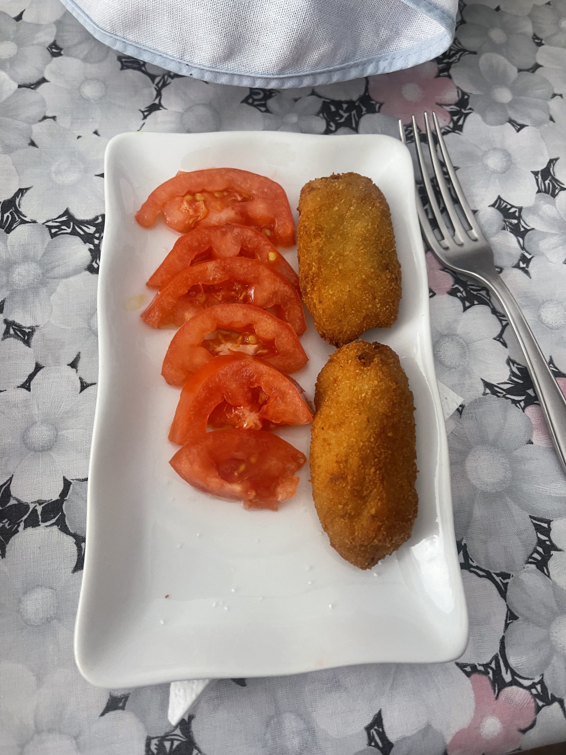 A picture of a plate with two fried croquetas of chicken and sliced tomato.